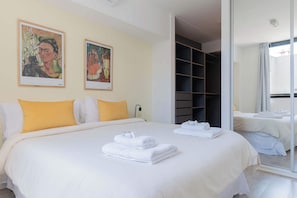 Habitación de hotel con una cama grande, dos cuadros en la pared, un armario y un baño visible a través de una puerta de cristal.