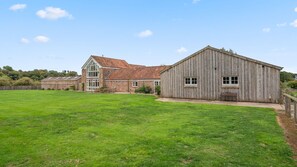 A large, open grassy area with a stone building and a wooden barn.