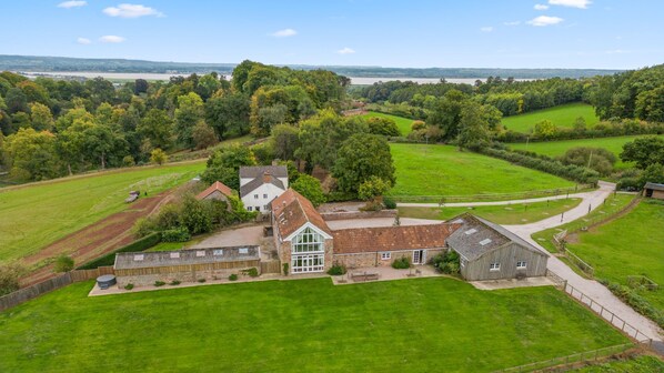 A large house with a spacious lawn, a driveway, and a view of a river in the distance.