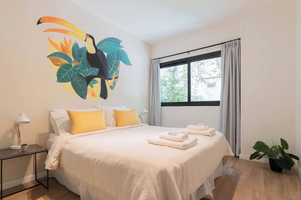 A hotel room with a bed, a nightstand, a window, and a wall mural.