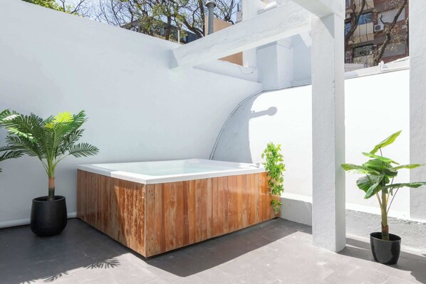 A modern outdoor hot tub area with a wooden exterior, surrounded by white walls and potted plants.
