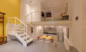 A modern apartment with a staircase leading to a loft bedroom, a dining area, and a kitchenette.