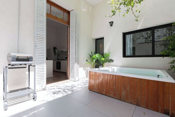 A modern bathroom with a wooden bathtub, a glass-enclosed shower, and a cart with a heater.