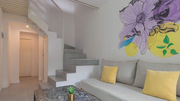 Un intérieur moderne avec un escalier, un canapé agrémenté de coussins jaunes et un mur orné d’une grande fresque florale.