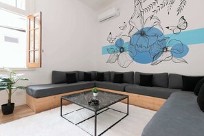 Un salon moderne avec un canapé d’angle, une table basse en verre et une fresque murale représentant des fleurs et des papillons.
