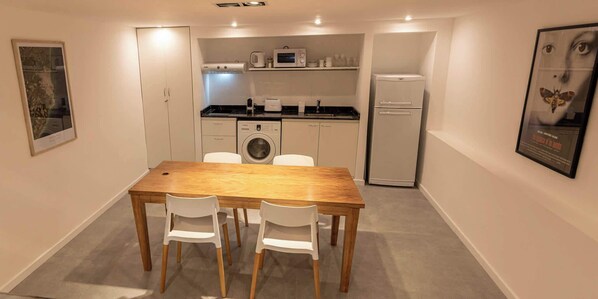 Una cocina compacta con una mesa y sillas de madera, lavadora, microondas y refrigerador.