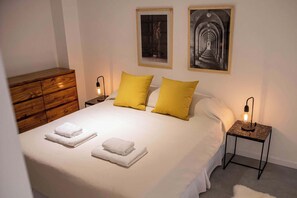 A neatly made bed with white linens and two yellow pillows, a wooden dresser, and two bedside tables with lamps.