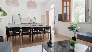 Une cuisine moderne avec des appareils électroménagers blancs, un coin repas avec des chaises noires et une grande fenêtre donnant sur un paysage verdoyant.