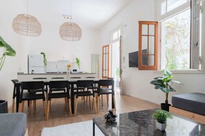 Een moderne keuken met witte apparaten, een eetgedeelte met zwarte stoelen en een groot raam met uitzicht op groen.