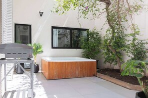 A modern outdoor area with a wooden hot tub, a grill, and potted plants.