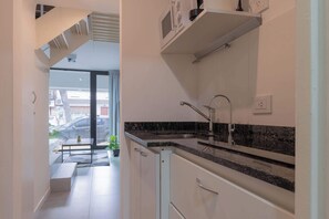 A modern kitchen with a granite countertop, stainless steel sink, and white cabinetry. There is a staircase leading to an outdoor area with a railing and potted plants.