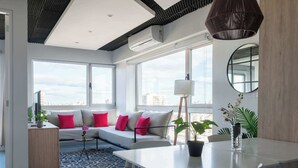 Ett modernt vardagsrum med en soffa, ett matbord och stora fönster med utsikt över staden.