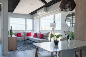 A modern living room with a sofa, dining table, and large windows offering a city view. - MOT Rentals + Madero Azopardo 'B' Lux Lofts Pool (Puerto Madero)