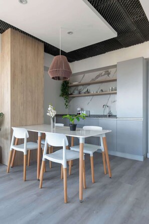 Una cocina moderna con salpicadero de mármol, una zona de comedor con mesa y sillas blancas, y una lámpara colgante.