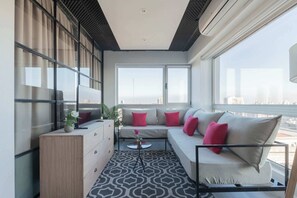 Una sala de estar moderna con un sofá, una mesita de centro y un armario. Se observan ventanas amplias con vistas a la ciudad.