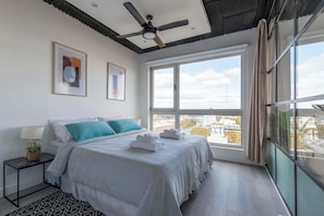 A modern hotel room with a large bed, a ceiling fan, and a city view through the window.