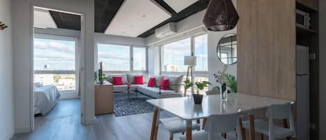 A modern living room with a dining area, large windows, and a city view.