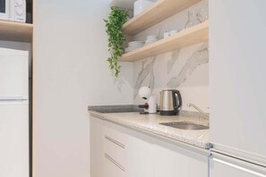 Une cuisine moderne avec des meubles blancs, un plan de travail en granit, une machine à café et un évier.