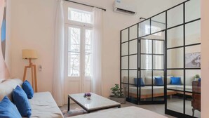 A room with a bed, a sofa, a table, and a sliding glass door leading to a balcony.
