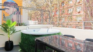 A rooftop terrace with a hot tub, a table, chairs, and a mural.