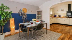 A dining area with a table set for two, a decorative wall with nautical elements, and a kitchen in the background. - English Riviera Coastal Holiday Home in Devon Uk (Paignton)