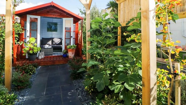 A wooden pergola with a red roof and a seating area with a bench and cushions. - English Riviera Coastal Holiday Home in Devon Uk (Paignton)