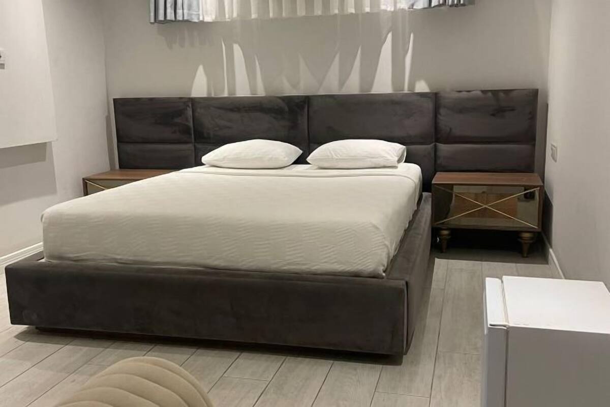 A modern bedroom with a large bed, two bedside tables, and a small wooden nightstand.