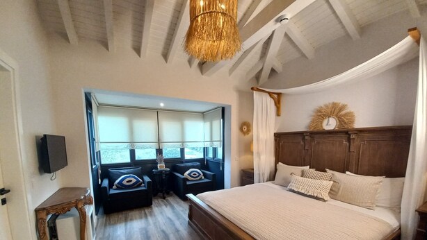 A bedroom with a large bed, wooden headboard, and a canopy. There are two armchairs and a small table with decorative pillows. - Chloe Alacati (Cesme)