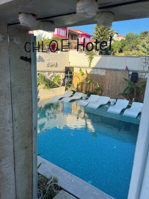 Zona de piscina con sillas de descanso, un muro de piedra y vistas a edificios coloridos al fondo.