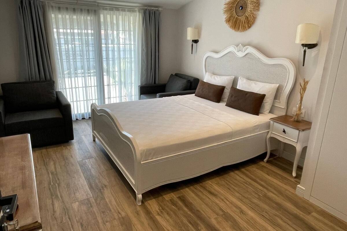 A hotel room with a large bed, a sofa, a desk, and a window with curtains.