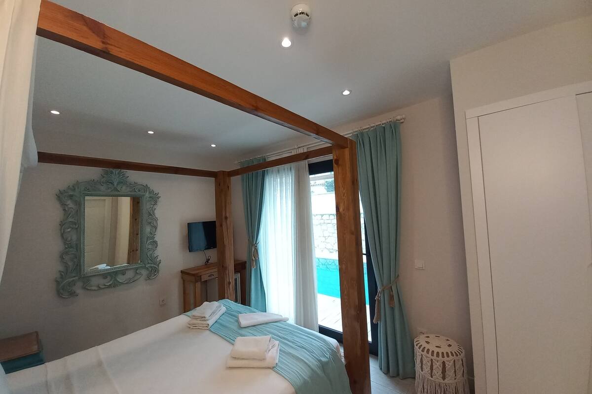 A bedroom with a bed, a mirror, a television, and a window with curtains.