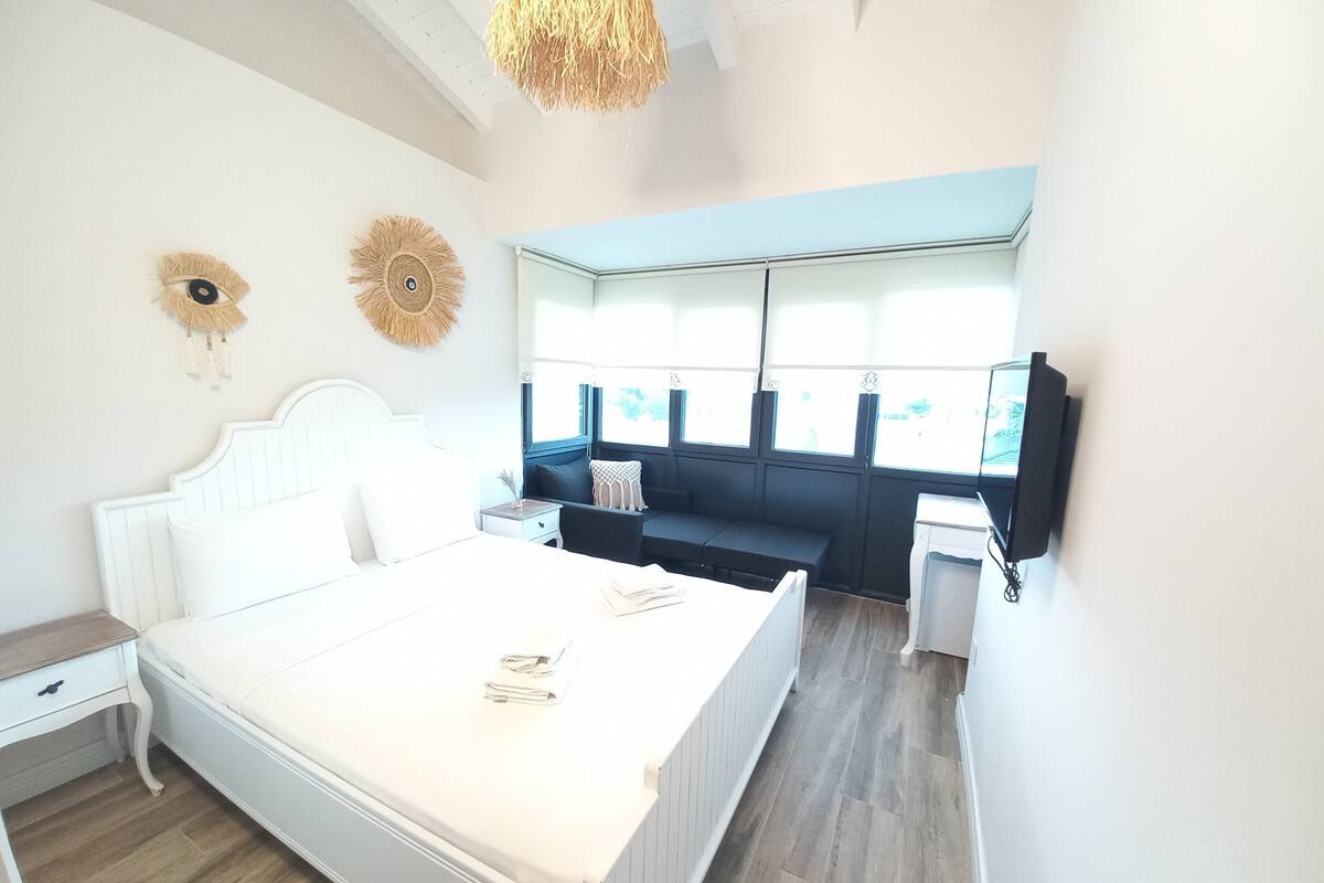 A bedroom with a bed, bedside table, nightstand, and a window with a view.