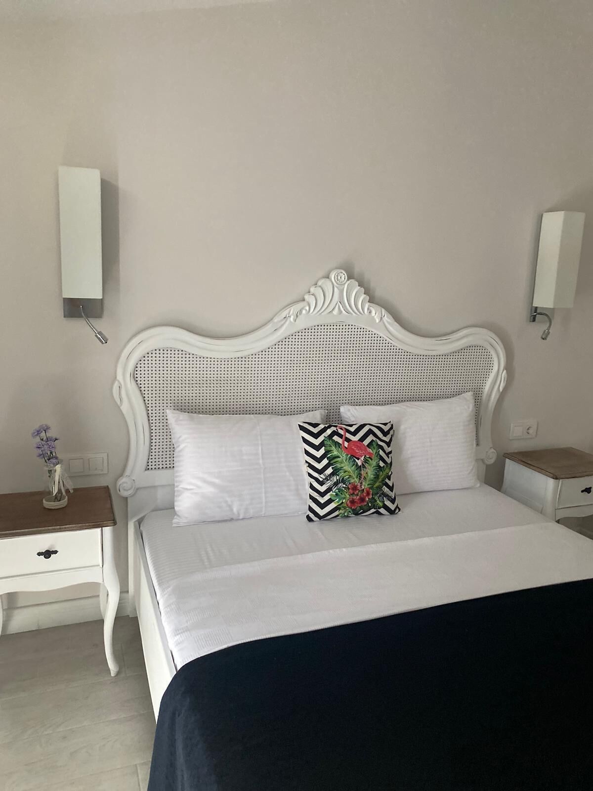 Un lit bien fait, avec une tête de lit blanche, deux tables de chevet et un luminaire fixé au mur.