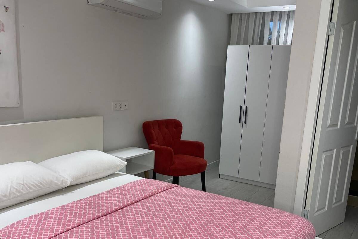 A modern bedroom with a bed, a red chair, a wardrobe, and an air conditioning unit.