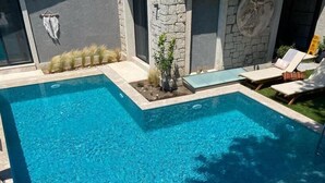 A swimming pool with clear blue water, surrounded by lounge chairs and potted plants. - Chloe Alacati (Cesme)