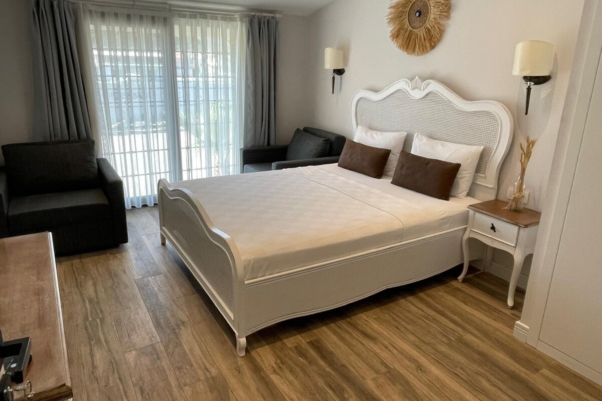 A hotel room with a large bed, a sofa, a desk, and a window with curtains.