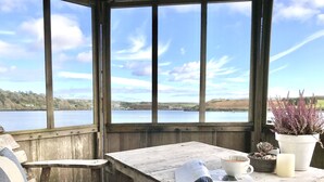 A wooden deck with a table and chairs overlooking a lake. - Adults-Only Waterfront Guest Suite | Stunning Harbour Views | Cozy Fireplace (Kinsale)