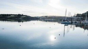 A calm marina with boats docked, a clear sky, and a hilly landscape in the background. - Adults-Only Waterfront Guest Suite | Stunning Harbour Views | Cozy Fireplace (Kinsale)