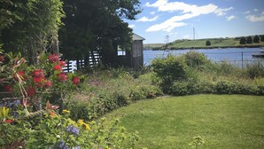 A garden with a variety of plants and flowers, a wooden fence, and a view of a lake with boats. - Adults-Only Waterfront Guest Suite | Stunning Harbour Views | Cozy Fireplace (Kinsale)