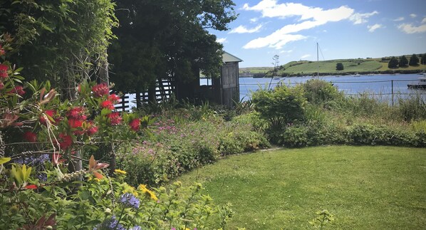 A garden with a variety of plants and flowers, a wooden fence, and a view of a lake with boats.