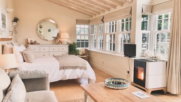 A cozy bedroom with a bed, bedside table, and a fireplace. - Adults-Only Waterfront Guest Suite | Stunning Harbour Views | Cozy Fireplace (Kinsale)