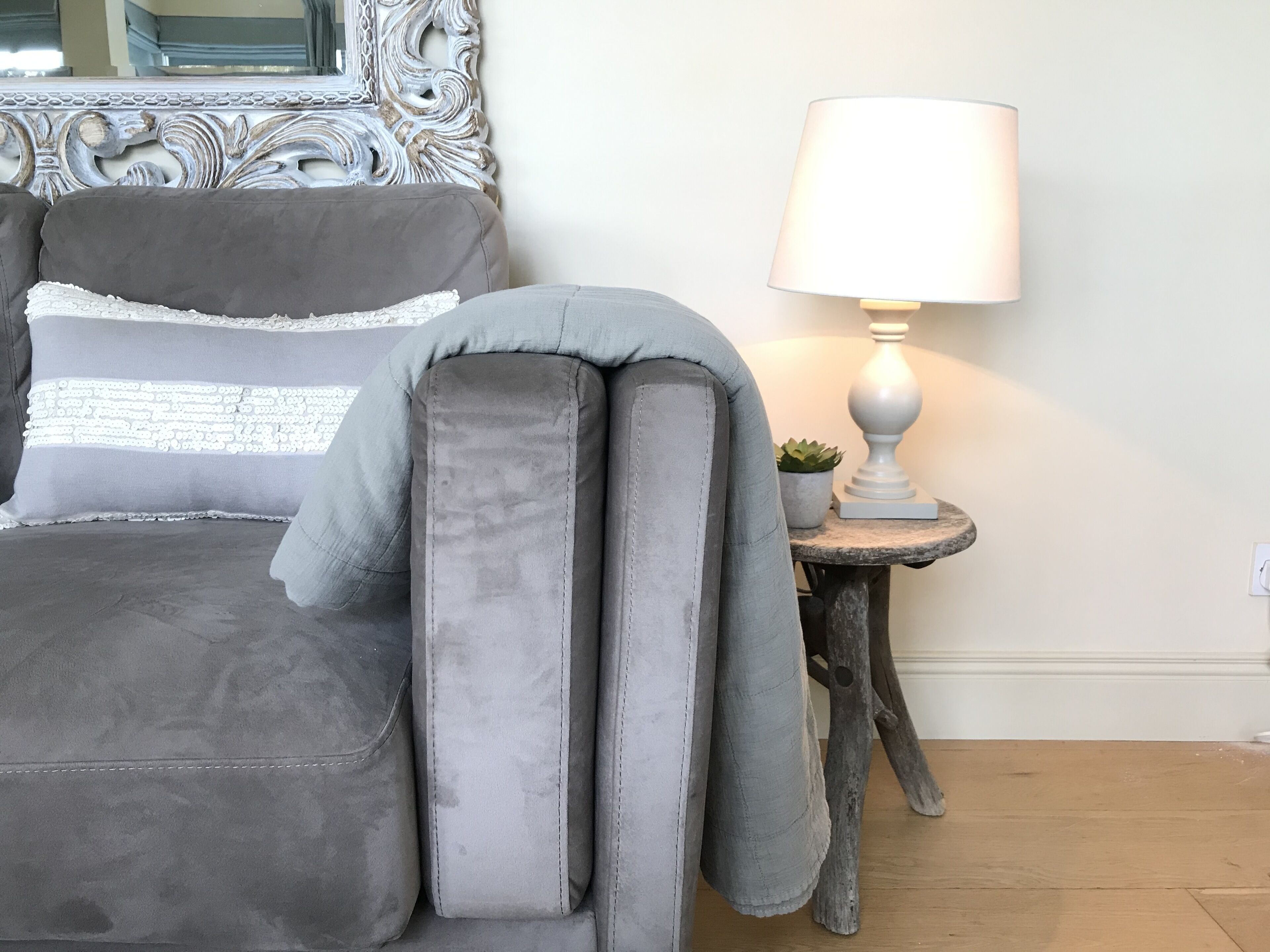 Un lit avec une literie grise, une tête de lit décorative, une lampe de chevet et une petite plante en pot posée sur une table de chevet en bois.