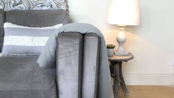 Un lit avec une literie grise, une tête de lit décorative, une lampe de chevet et une petite plante en pot posée sur une table de chevet en bois.