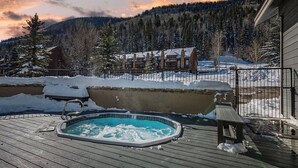 A wooden deck with a hot tub, a bench, and a view of a lodge in a snowy mountainous area. - Silver Vista End Unit | Pool & Ski Shuttle, Hot Tub, Fireplace, Balcony (Durango)