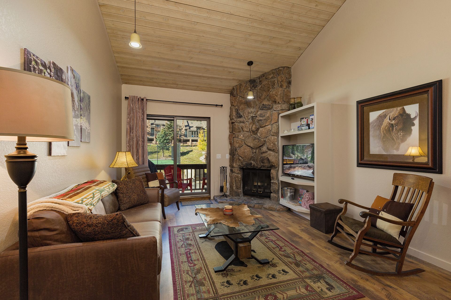 A cozy living room with a stone fireplace, a sofa, a glass coffee table, and a rocking chair.