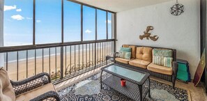 A balcony with a view of the beach, wicker furniture, and a patterned rug.
