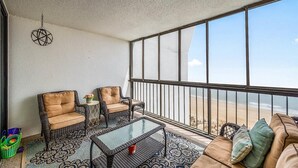 Un balcón con mobiliario de mimbre, una mesa de vidrio y vista a la playa.