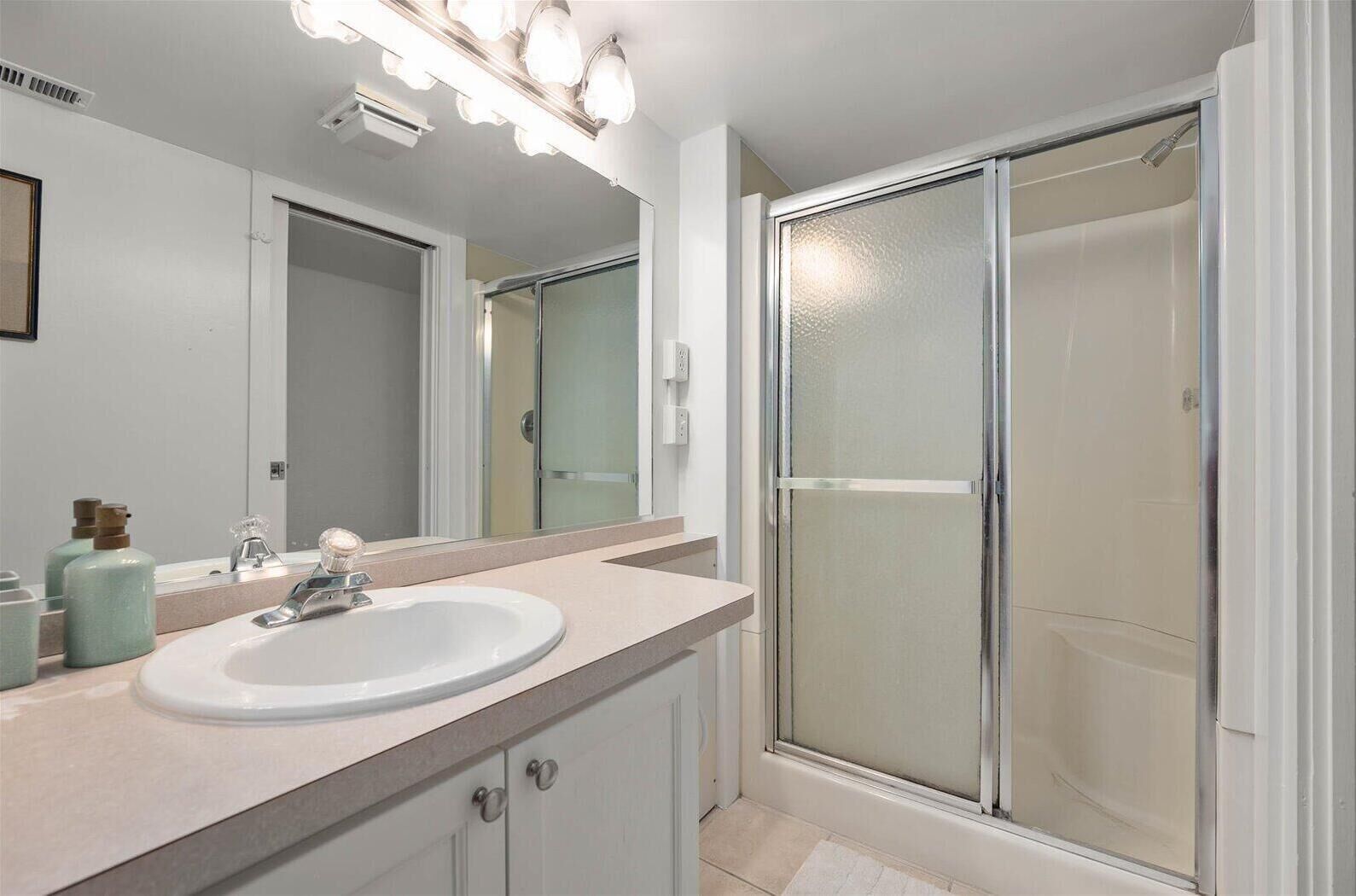 A bathroom with a white sink, a mirror, and a glass shower enclosure.