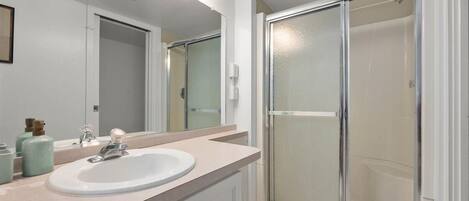 A bathroom with a white sink, a mirror, and a glass shower enclosure.