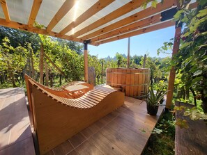 Een houten terras met een hangmat, een houten vat en een pergola met lichtslingers.